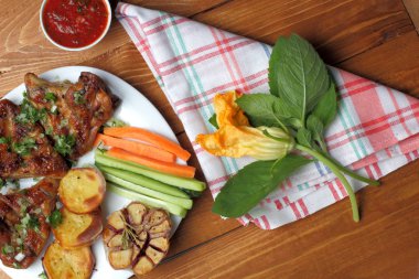 Yakın çekim, kızarmış tavuk kanatları, pişmiş patates ve sarımsak, doğranmış taze sebzeler, kabak çiçekleri, nane lahanası, baharatlı domates sosu ile bir plaka üzerinde üst görünüm.