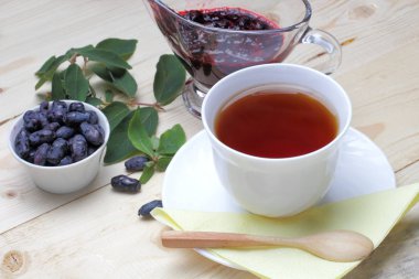 Reçel ile taze hanımeli meyveleri, ahşap bir masada bir fincan çay. Hafif rustik kahvaltı.