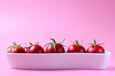 Pembe arka plan üzerinde küçük bir seramik standında Kiraz domates, metin için yer, parlak doğal kırmızı renk, yüksek kontrast.