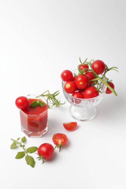 Yeşil sprigs ve beyaz bir arka plan üzerinde taze domates suyu bir bardak ile Parlak kiraz domates. Parlak doğal renkler, yüksek kontrast.