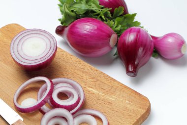 Kesme tahtasındaki kırmızı soğan halkaları ve maydanozlu tam soğan..