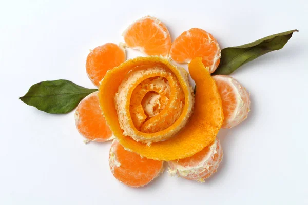 Slices of mandarin oranges and citrus peel in the form of a flower with green leaves on a white background, original shape.