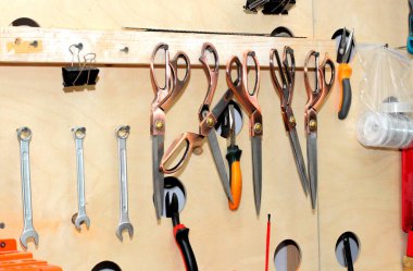 Ahşap bir duvarda çeşitli aletler asılı. Makas, anahtarlar, bant makarası, tornavida, tel kesici, mandallar..
