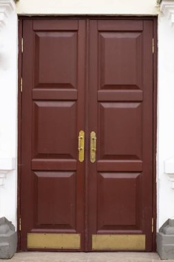 Duble koyu büyük ahşap giriş kapısı ve taş bir binanın duvarında bronz sapları var..