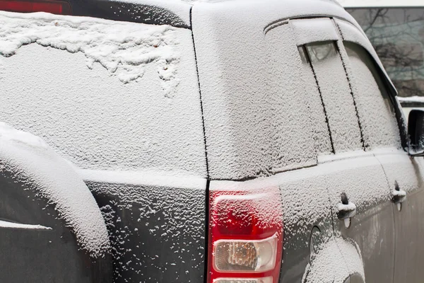 The cars in the parking lot are covered with the first snow, a concept of a snowy or early winter.