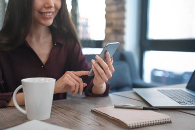 Cep telefonu arka planda çalışan kız ile fincan kahve, defter ve laptop masası yakın çekim
