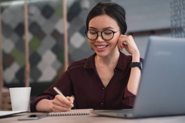 İşkadını bilgileri not defterinde oturma ve bildirimi. Asyalı kadın yönetici gözlük coworking ve yazım kalemi ile bazı ayrıntıları, oturma