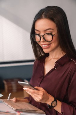 Neşeli kadın yönetici olarak not ile cep telefonu Mesajları okuma gözlüğü kitap elinde 