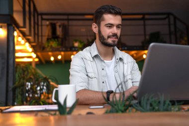 Beyaz gülümseyen iş adamı coworking içinde bilgisayar üzerinde çalışıyor. Genç erkek Müdürü fincan kahve ile ayarlıyoruz onun masaüstü bilgisayar ve Not defteri ile üzerinde oturuyor