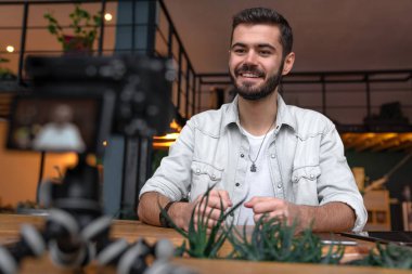 Genç adam onun abonelerine konuşurken kameraya bakıyor. Masasının üzerindeki onun kamera ile genç blogger