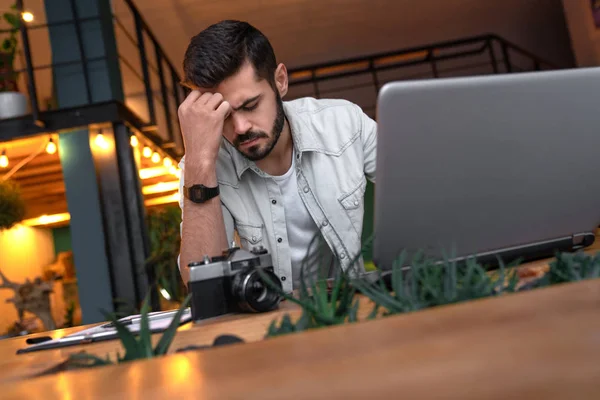 办公室里压力大的年轻商人 沉思的年轻人坐在工作场所 上面有笔记本电脑和数码相机 — 图库照片