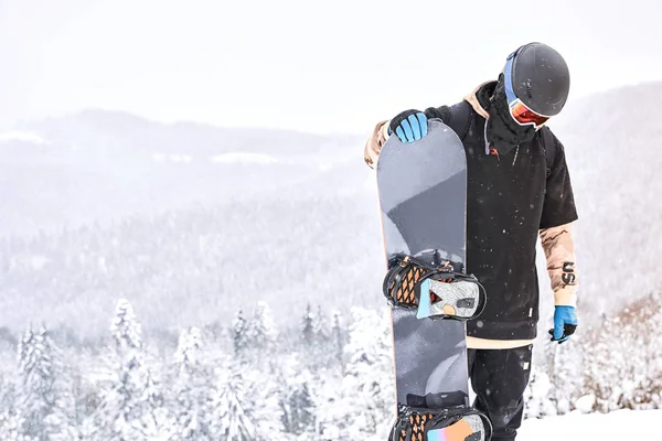 Manliga Snowboardåkare Tittar Hans Snowboard Kulle Med Berg Och Forrest — Stockfoto