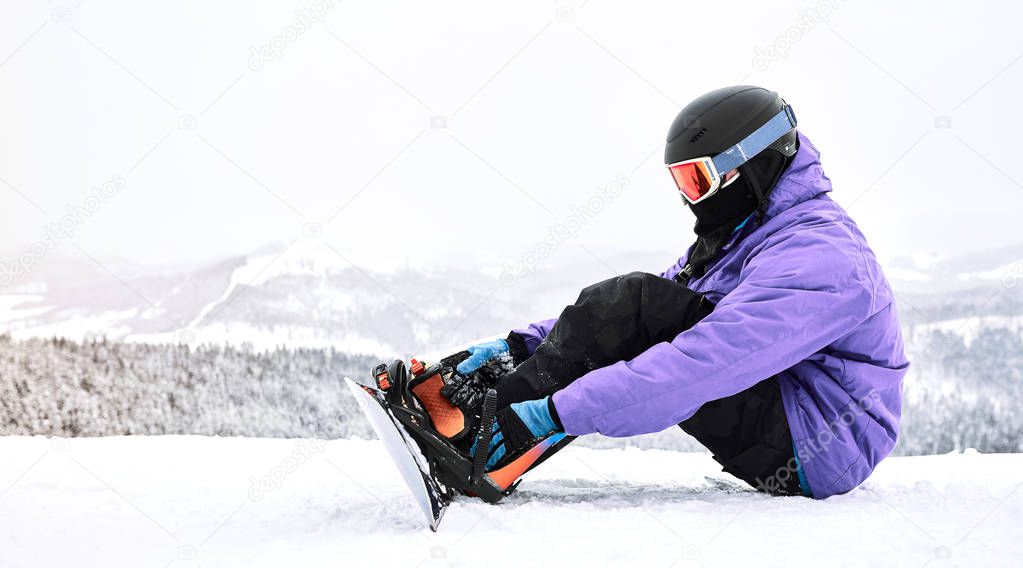  Checking equipment. Snowboarder sit down to check his board and mounts before continue downhill                              