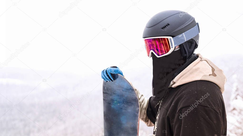 Snowboarder portrait that hold snowboard standing on top of hill and looking for a ride with mountain on the background                               