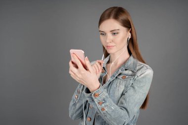 Video çağrısı tarafından cep telefonu üzerinde gri arka plan üzerinde duran kulaklık ile konuşurken denim ceket genç kadının yatay atış