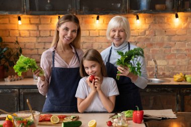 Güzel aile sebze ellerinde kamerayla salata mutfakta yemek yaparken poz gülümseyen