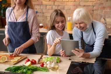 Kadın kıdemli portresi bu tablet torunu ile seyir ve gülümseyerek. Anne mutfakta yemek
