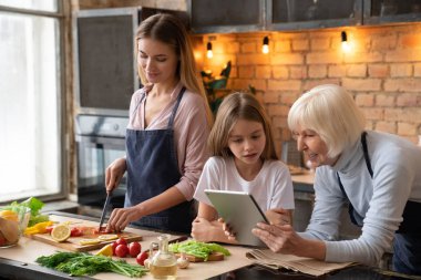Bu onun torunu ile tablet looking üst düzey kadın vurdu ve gülümseyen yatay. Vegetatian yemek mutfakta anne