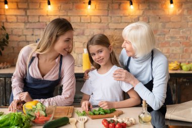 Üç kuşak aile mutfak birlikte yemek. Sevimli küçük kız kamera bakışla salata kesme