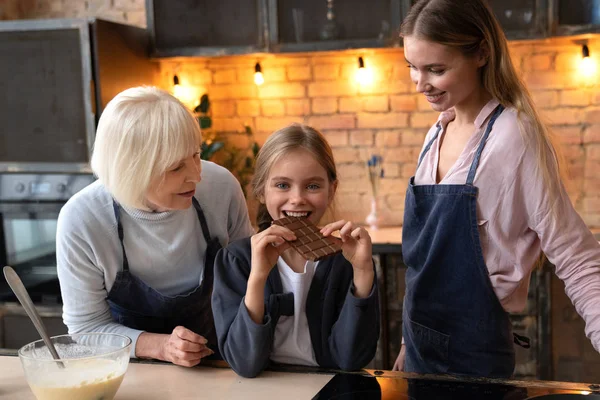 Niña Comiendo Chocolate Con Mirada Cámara Cocina Alegre Abuela Madre — Foto de Stock