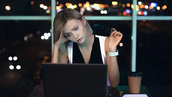 Something goes wrong. Young businesswoman with stress in the office late night. Female caucasian manager sitting at workplace with glasses in hand