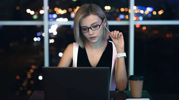 Gece geç saatlere kadar laptop üzerinde çalışan genç kadının ön görünümü. Beyaz iş kadını, ofis içinde çalışma tarihini, elinde kalemle bitirmek için fazla mesai yapıyor — Stok fotoğraf