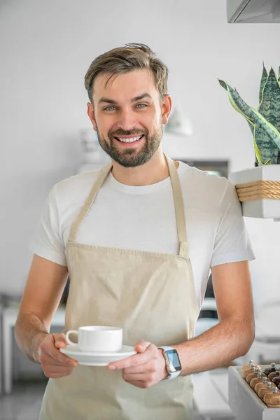 Függőleges lövés boldog kávézó tulajdonos jelentő egy kávéscsésze a kezében. Closeup a Barista állt a bejáratnál a kávézóban tartó kávéscsésze. — Stock Fotó