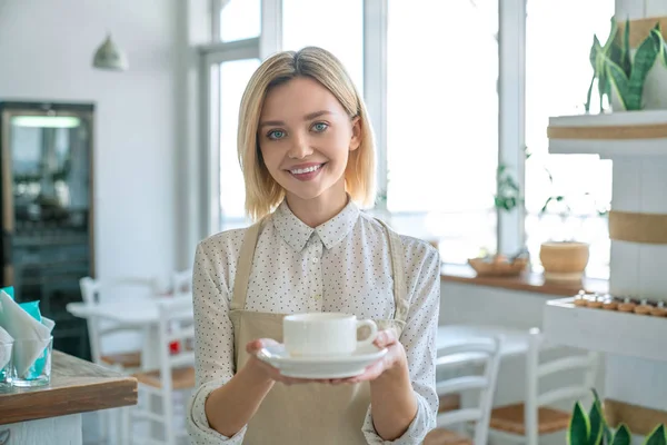 Lachende vrouw die koffie in een koffieshop serveert. Happy Coffee shopeigenaar houdt een kopje koffie in de winkel. — Stockfoto