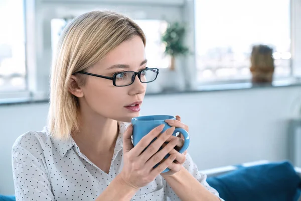 Retrato de mulher jovem atraente consciente sentado à mesa do café com xícara de café na mão. Jovem empresária caucasiana tomando café no coffeeshop — Fotografia de Stock