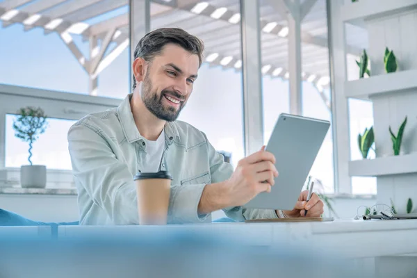 Homem sorridente trabalhando em seu tablet digital em uma cafeteria . — Fotografia de Stock