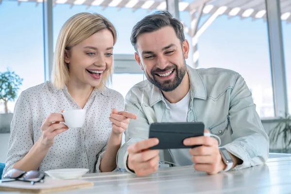 Casal sorrindo tirando uma selfie usando telefone celular. Homem e mulher compartilhando momentos felizes em um café enquanto assiste vídeo no smartphone usando fones de ouvido — Fotografia de Stock