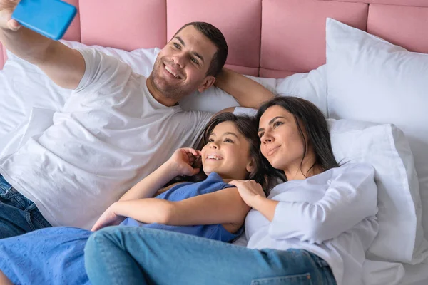 Boldog fiatalember figyelembe selfie családjával. Családi feküdt az ágyban, és figyelembe selfie otthon — Stock Fotó