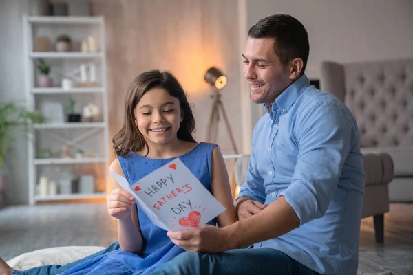 ¡Feliz Día del Padre! Caucásico joven hombre en casa con su pequeña linda chica mira a regalo postal — Foto de Stock