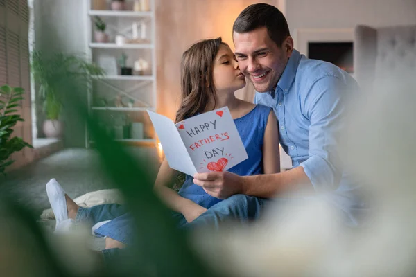 С Днем отца! Милая маленькая девочка целует своего отца и дарит ему подарочную открытку — стоковое фото