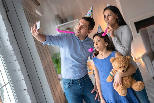Feliz familia celebrando un cumpleaños juntos en casa. Hombre tomando selfie en el teléfono inteligente con la mujer atractiva hormiga su linda hija —  Fotos de Stock