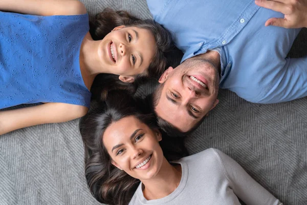 Concepto familiar feliz. Vista superior de la familia feliz de tres que se unen entre sí y sonriendo mientras están acostados en el suelo —  Fotos de Stock