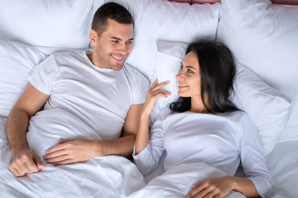 Χαρούμενο ρομαντικό ζευγάρι ξαπλωμένο στο κρεβάτι και γελώντας. Γυναίκα χαμογελά με τον άντρα της στο κρεβάτι και κοιτάζοντας ο ένας τον άλλο — Φωτογραφία Αρχείου