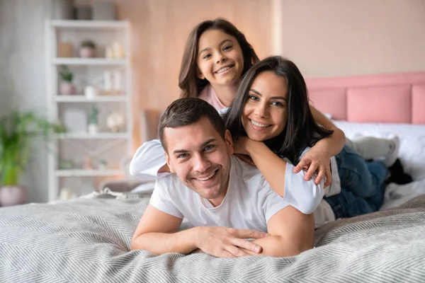 Genç ve güzel bir aile, kameraya bakarak yatakta yatarken birbirlerine sarılırlar. — Stok fotoğraf