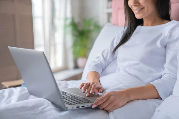 Vista lateral de la joven morena utilizando el ordenador portátil mientras está acostado en la cama en casa — Foto de Stock