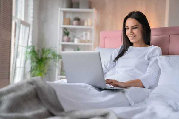 Οριζόντια βολή ελκυστική καυκάσιος γυναίκα που εργάζονται σε φορητό υπολογιστή, ενώ είναι στο σπίτι κρεβάτι — Φωτογραφία Αρχείου