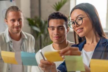 Post It notları ve çıkartmalar kullanarak cam duvar önünde tartışarak iş kadınların çekim yakın. Modern ofiste beyin fırtınası için yapışkan notlar kullanan kurumsal profesyoneller