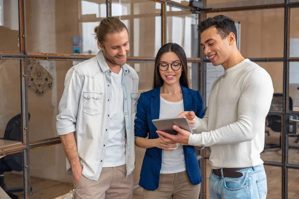 Three young business professionals standing together and discussing over business report in office hallway. Office colleagues revieving a business document on the tablet in coworking — Stock Photo, Image