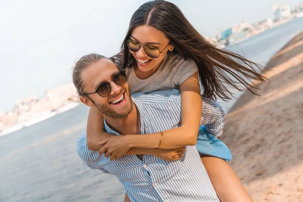 Romantik Genç çift yaz tatilleri zevk. Yakışıklı genç adam veren piggyback binmek için kız arkadaşı üzerinde plaj. — Stok fotoğraf