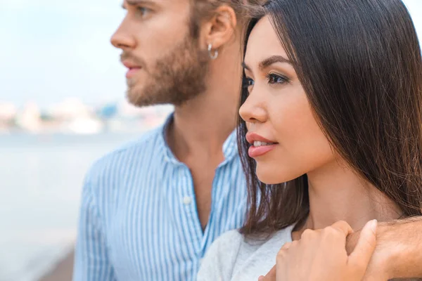 Närbild porträtt av ung man kramar sin flickvän på en sommardag. Par tittar på utsikt från stranden. — Stockfoto