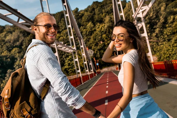 Hermosa joven pareja disfrutando de momentos juntos mirando a la cámara y sonriendo mientras camina al aire libre — Foto de Stock
