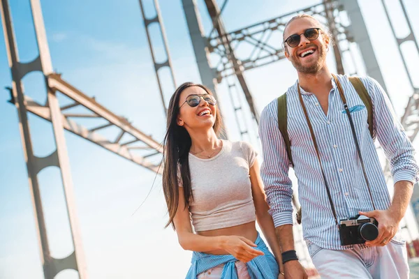 Tiro de alegre pareja joven feliz cogida de la mano mientras camina en el puente al aire libre — Foto de Stock