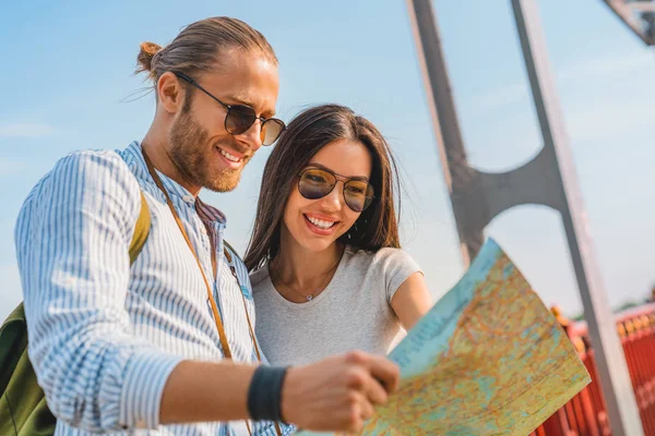 Vista lateral de la hermosa pareja joven mirando el mapa y sonriendo mientras está de pie al aire libre — Foto de Stock