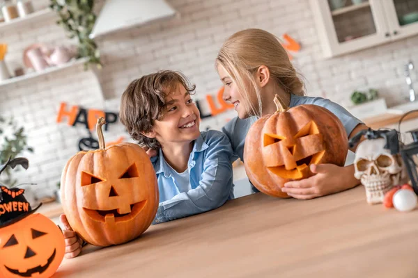 Young boy and his teenager sister having fun with pumpkins on Halloween at home kitchen — 图库照片