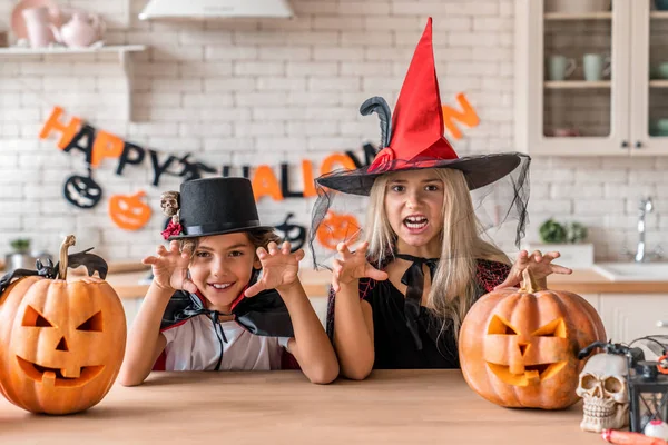 Crianças em ternos e com abóboras se divertindo no Halloween na cozinha da casa — Fotografia de Stock