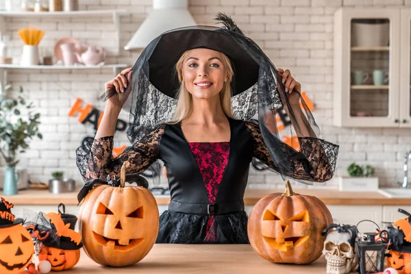 Glimlachende jonge vrouw staan in heks kostuum in Halloween versierde keuken — Stockfoto